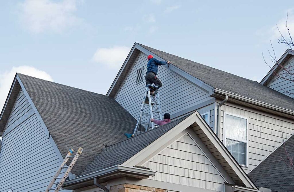 A comparison view of a house roof with half covered in gray asphalt shingles and half with standing seam metal panels.