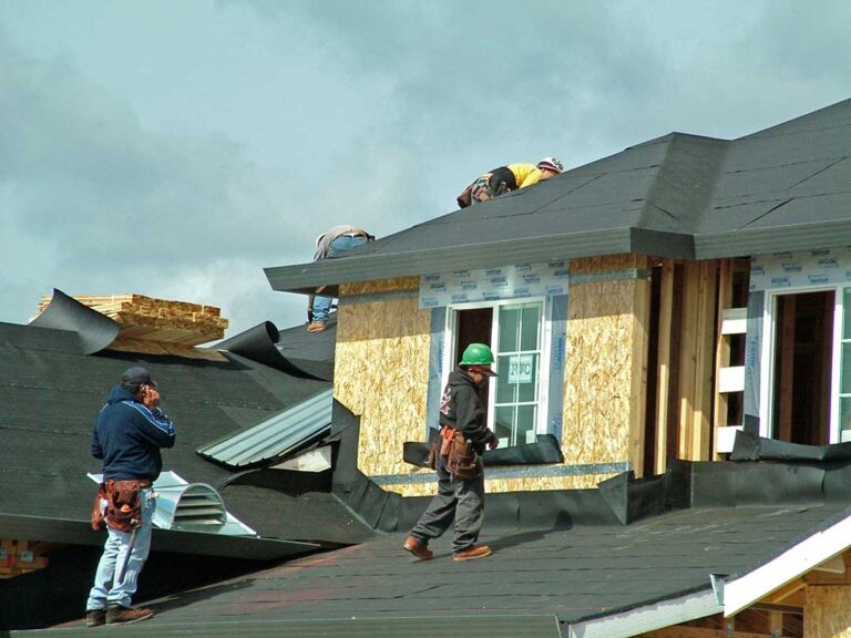 Person using a smartphone to photograph damaged roof shingles from their backyard after a storm.